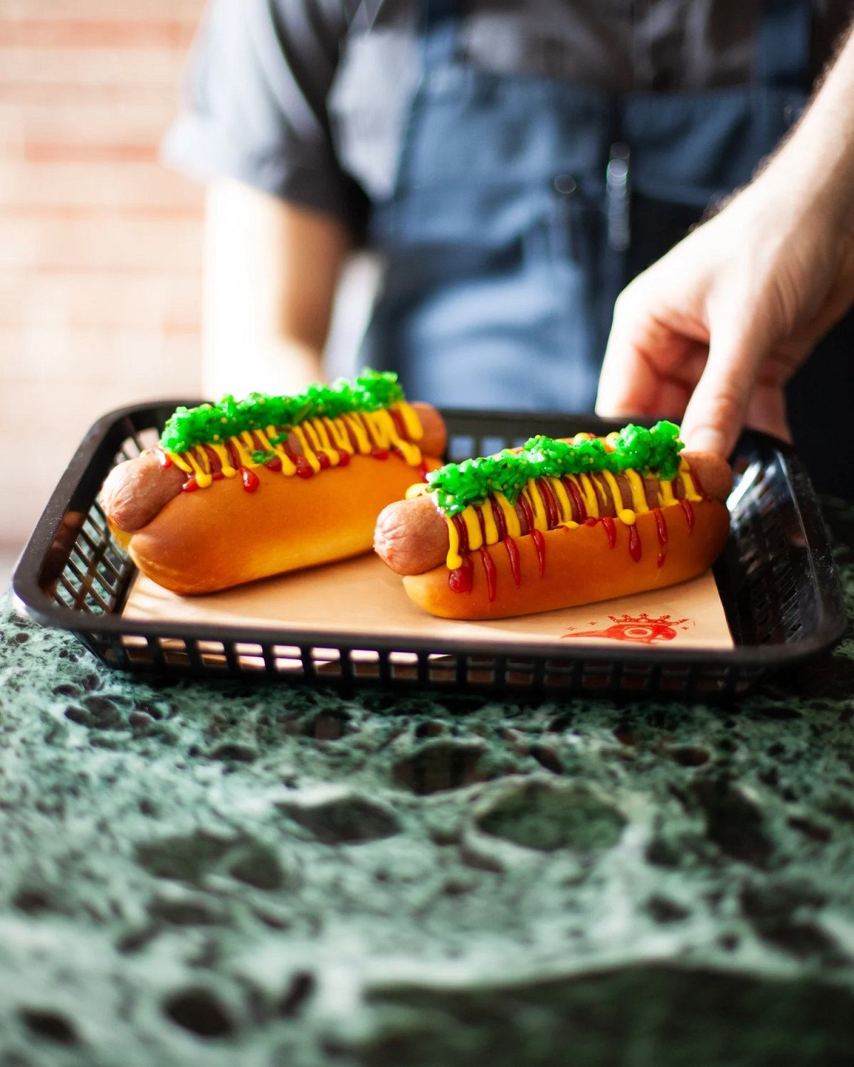Tray with two hot dogs topped with ketchup, mustard and green relish on table