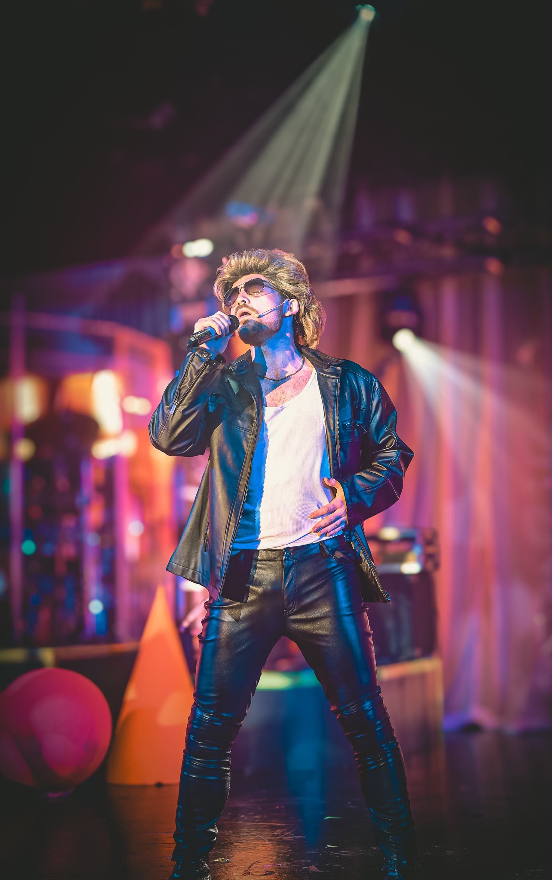 Performer in leather outfit singing under stage lights.