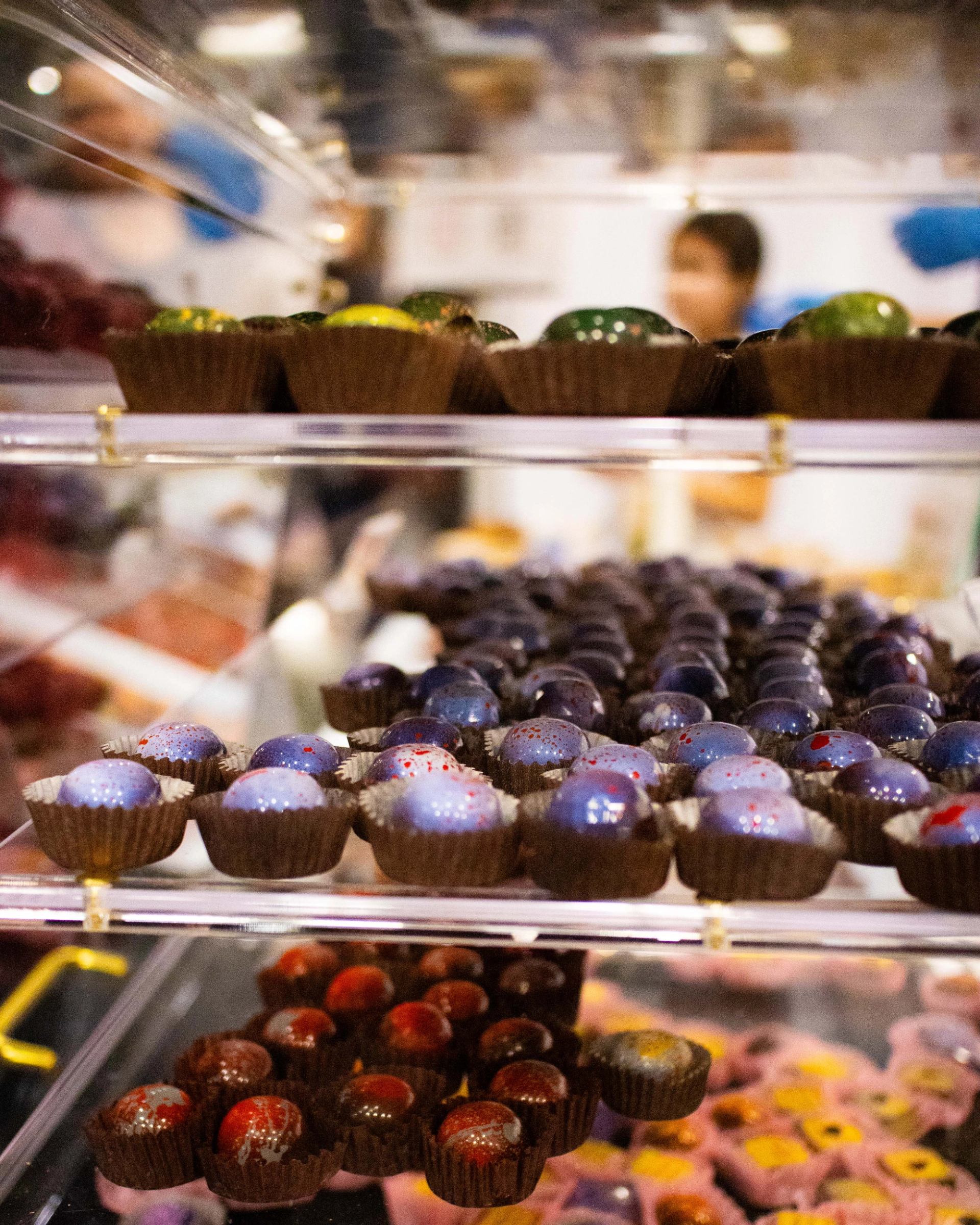 Display case with rows of colourful artisan chocolates in paper cups at a shop.