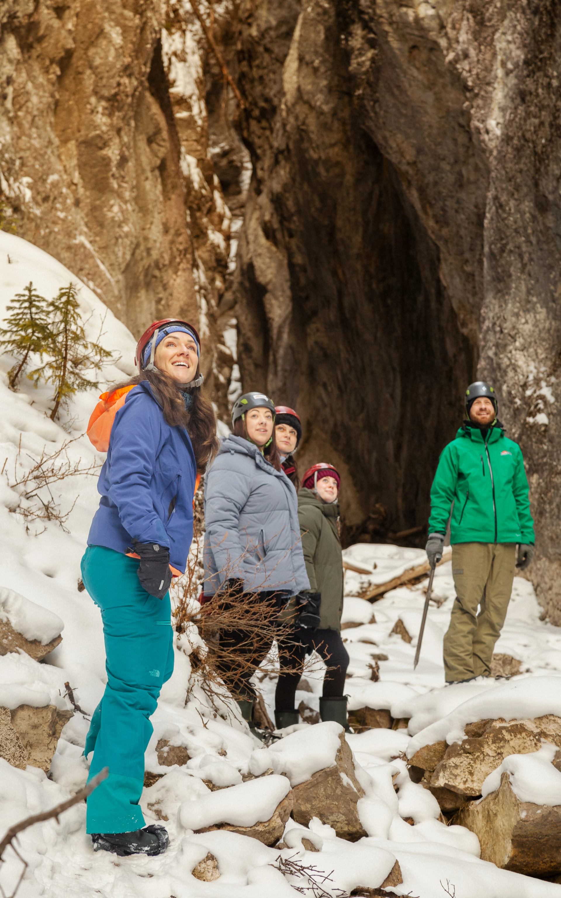 A group stands on snowy rocks near a narrow canyon surrounded by rugged winter mountain walls.