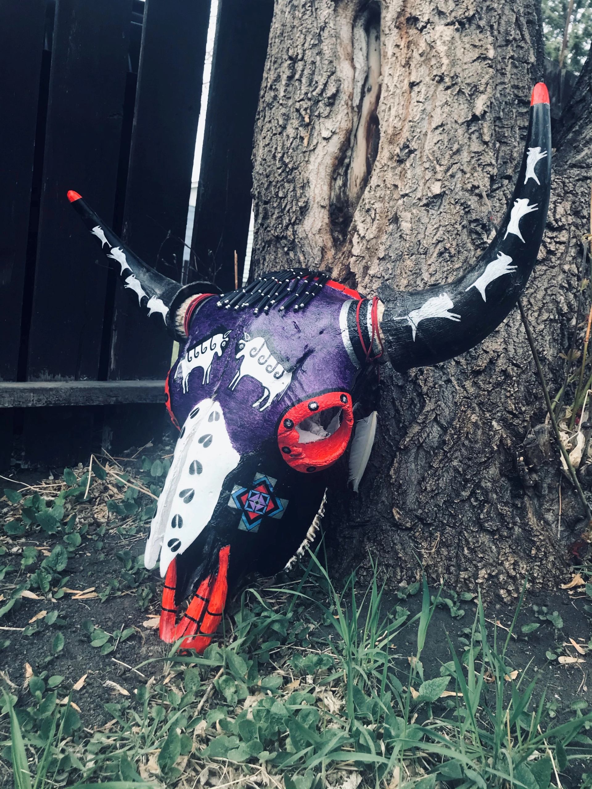Painted wooden moose figure with red-and-white patterns, leaning beside a rock wall.