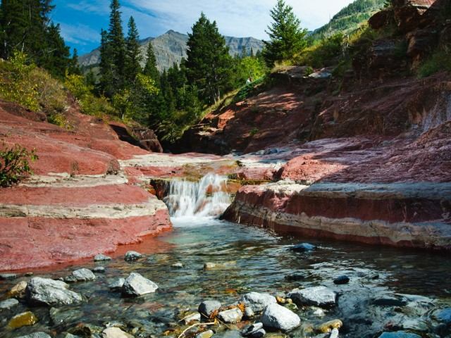 Rocky river valley with red cliffs, pine trees, and a small waterfall in Alberta’s Southern Rockies.