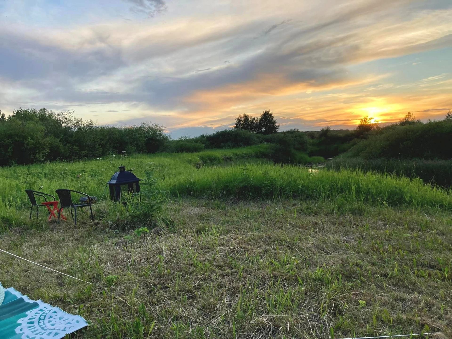 Chairs and firepit in grassy field with sunset and colorful sky