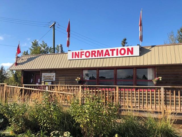 Visitor center with flags, flowers, and a wooden fence under a clear blue sky.