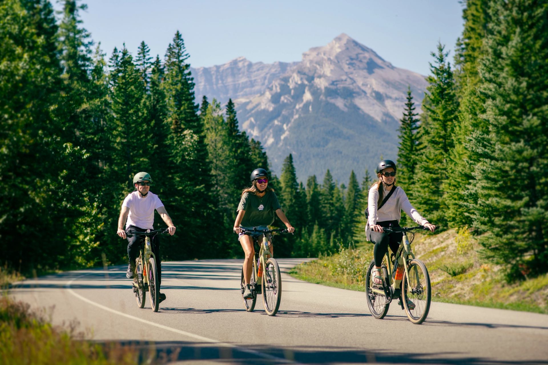 Three cyclists riding along a forested mountain road in Banff.