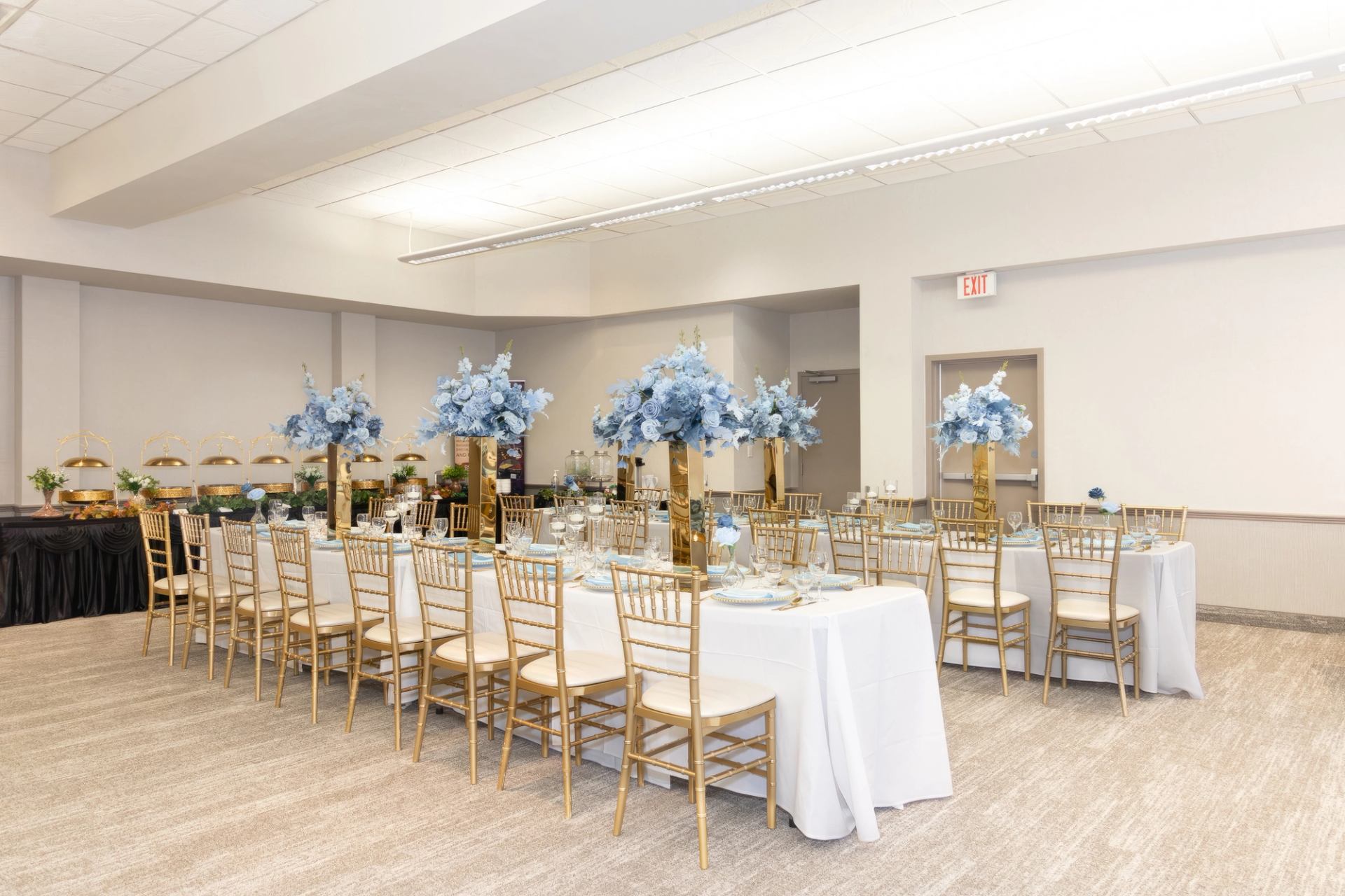 white and gold decor with blue florals on two long tables in one (of three) sections of event space