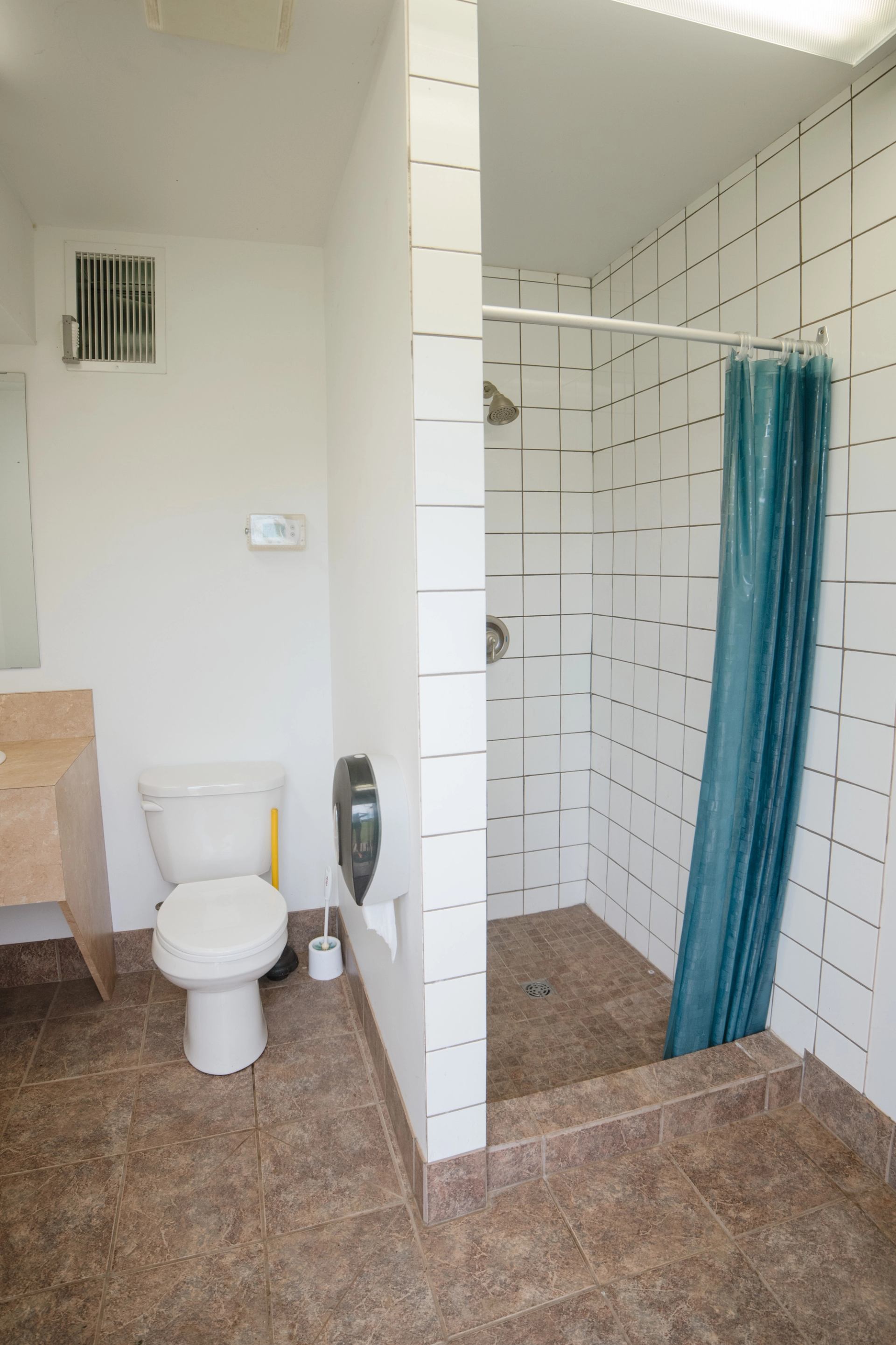 Tiled bathroom with toilet, wall-mounted sink, and open shower with blue curtain.