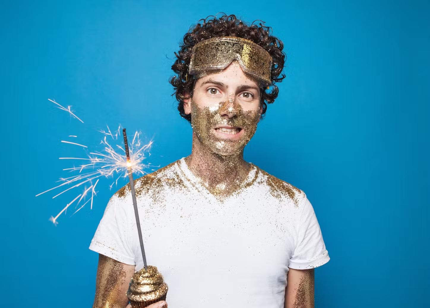 Man holding a sparker with sparks, wearing a white T-shirt against a blue background.