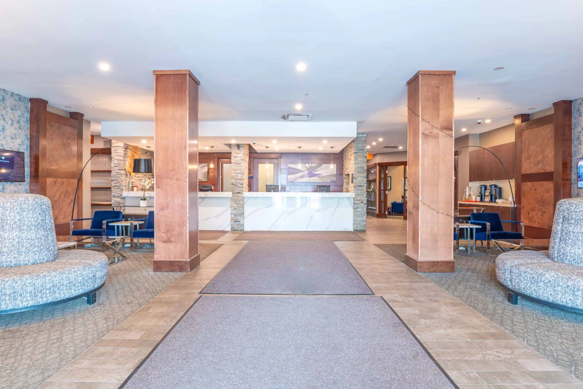 Hotel lobby with central front desk, tall columns, and seating areas.