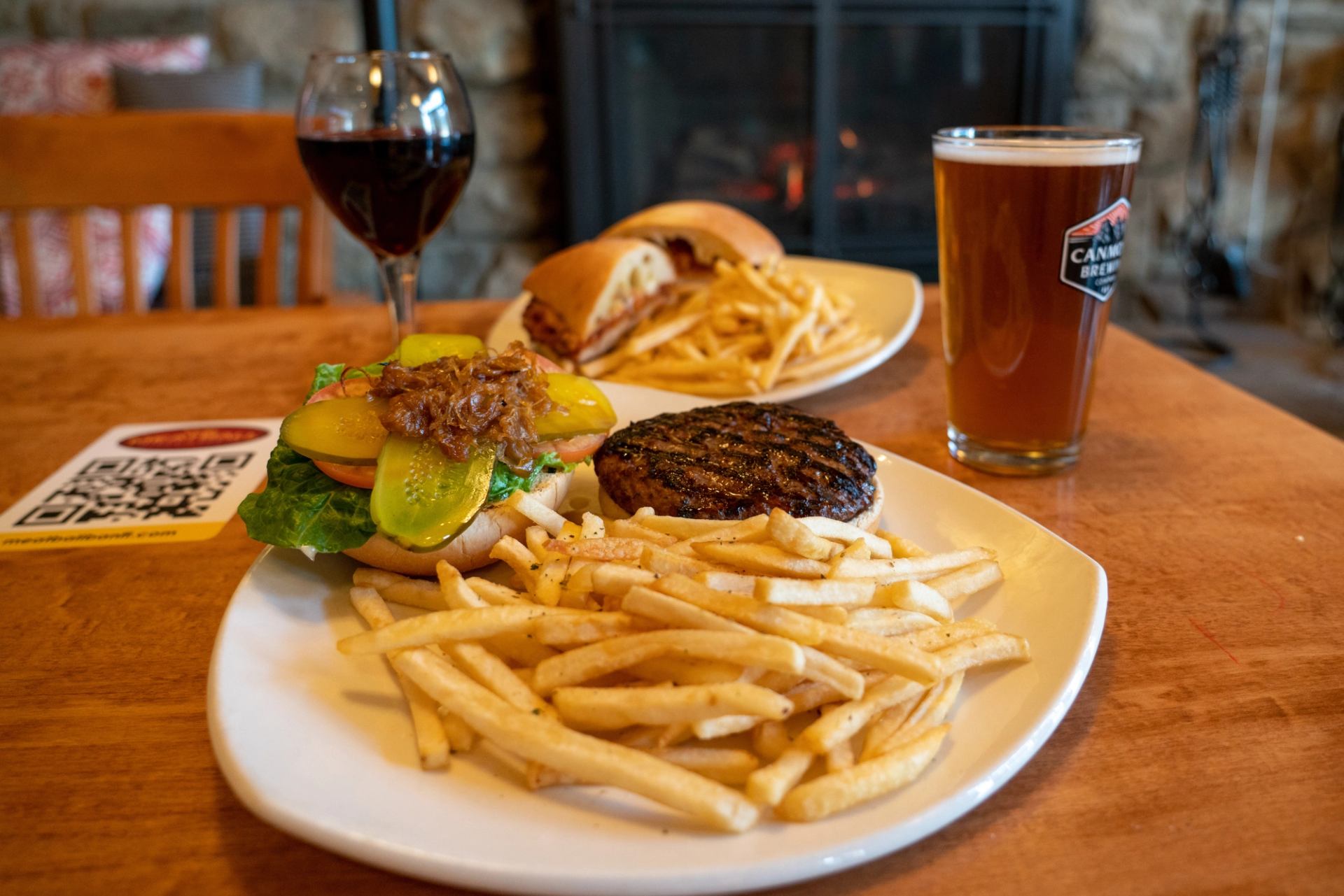 Plates of burgers, fries, wine, and beer in a cozy restaurant setting.