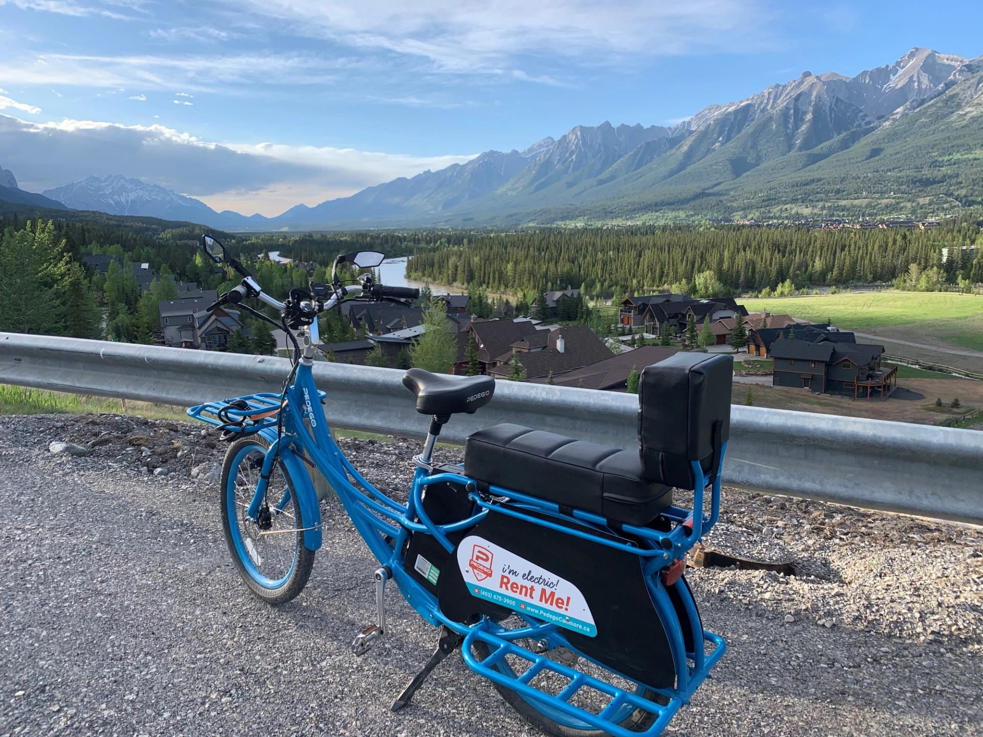 Blue electric bike parked by road with mountain views and green fields.