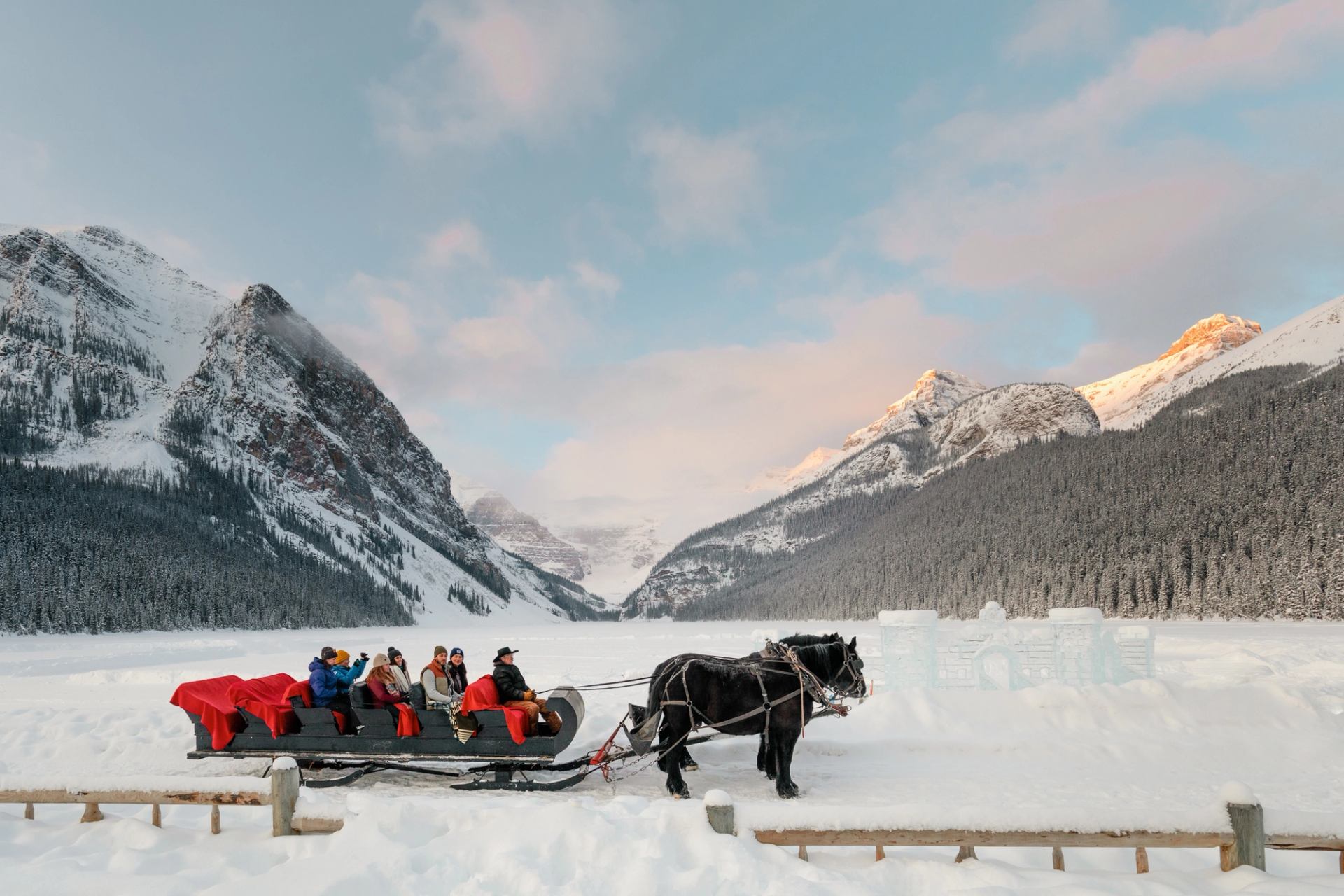 Horse-drawn sleigh carrying people through snowy mountains in Banff.