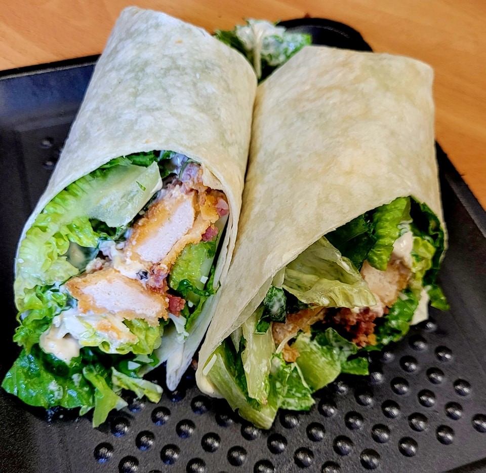 Chicken Caesar wrap cut in half on a black tray at Lakeview Bakery & Deli.