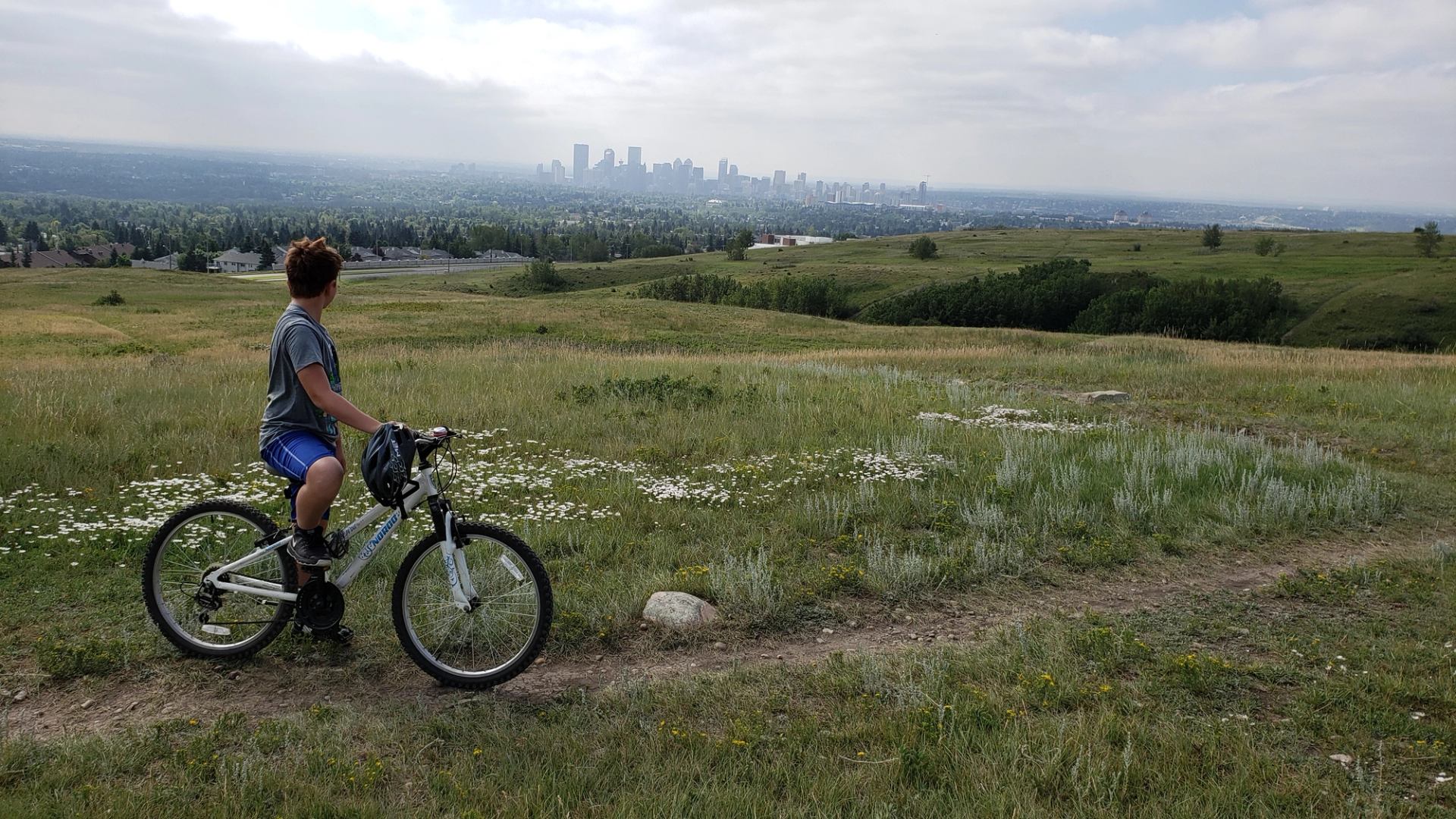 Boy with bike on trail at Nose Hill Park looking toward Calgary skyline