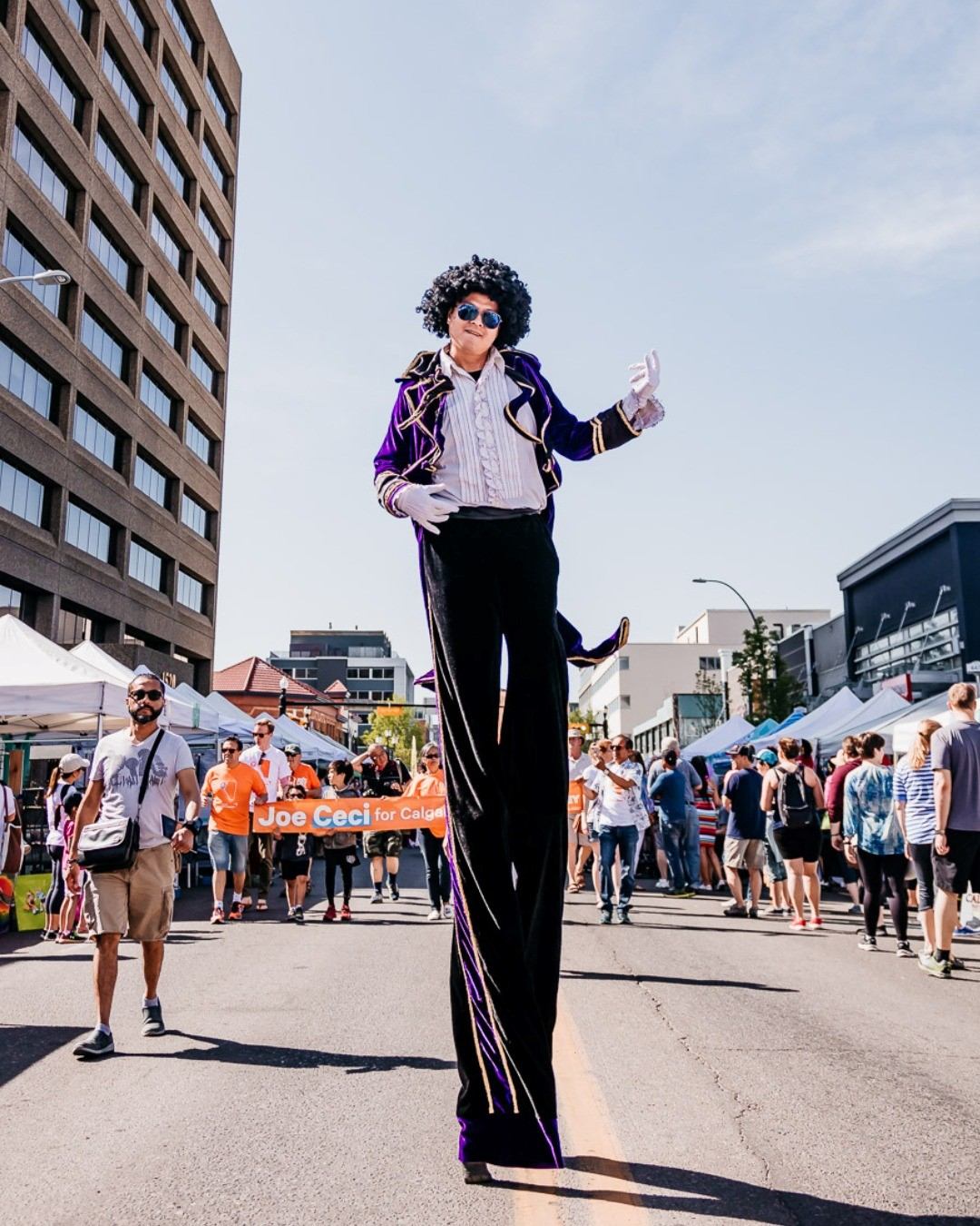 Tall street performer in a colorful outfit entertaining crowds at an outdoor festival.