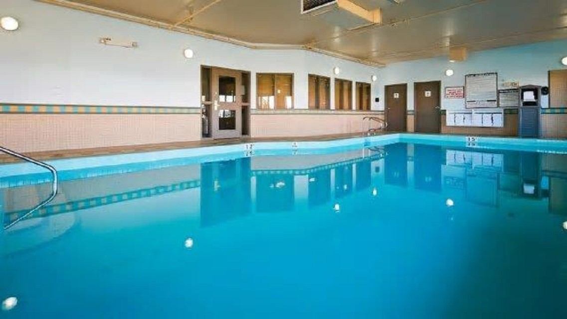 Indoor swimming pool with blue water and tiled wall, chairs and doors in background.
