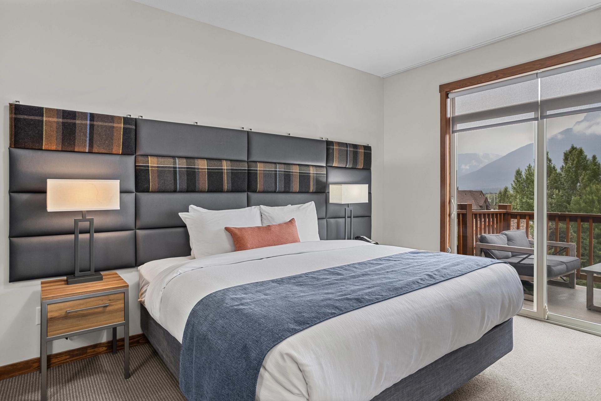 Bedroom with a large bed, padded headboard and balcony overlooking trees and mountains.