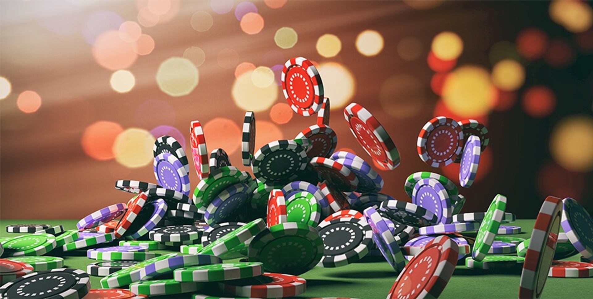 Colorful casino chips scatter and stack across a gaming table against sparkling lights.