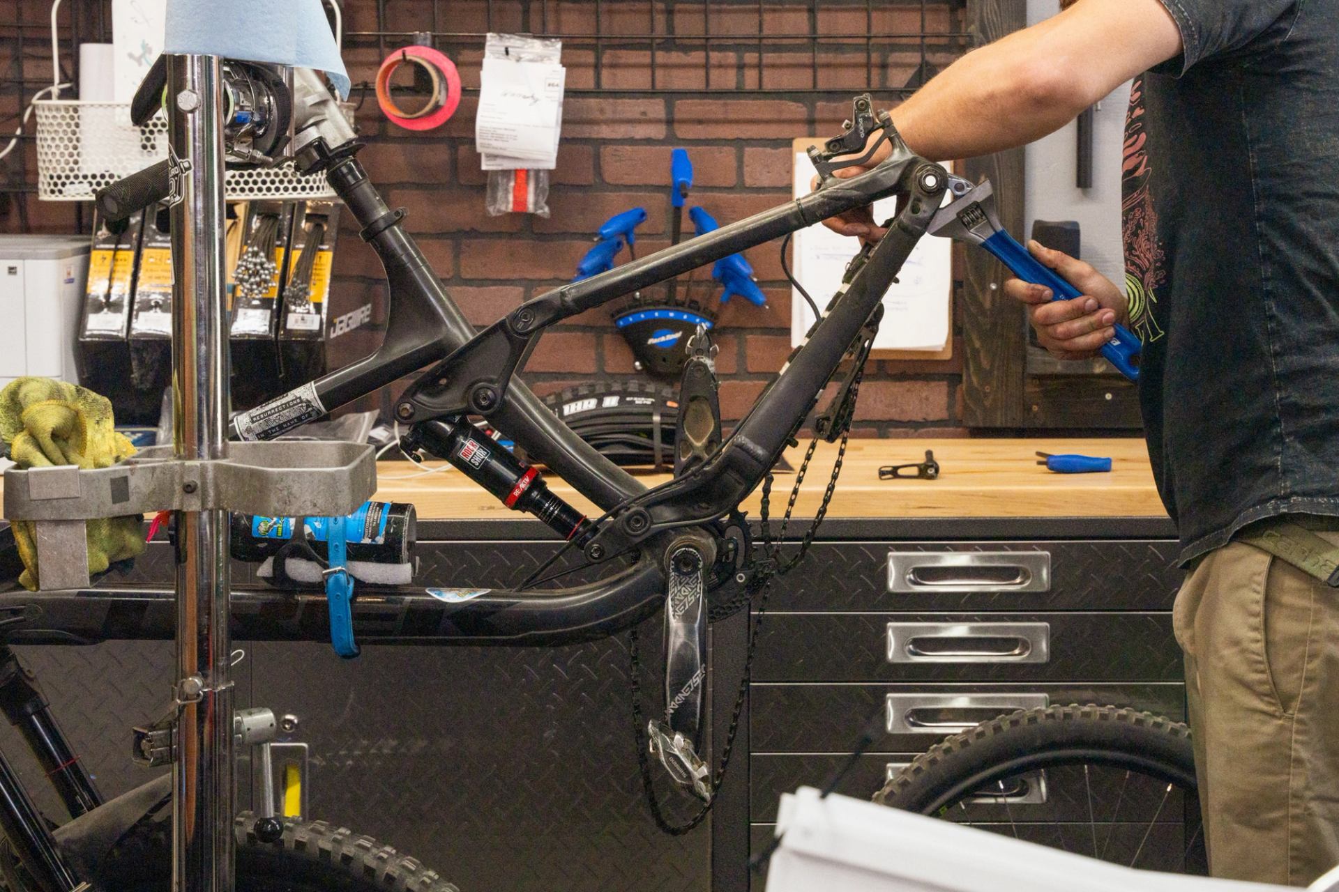 Person repairing a bike in a workshop with tools on the wall.
