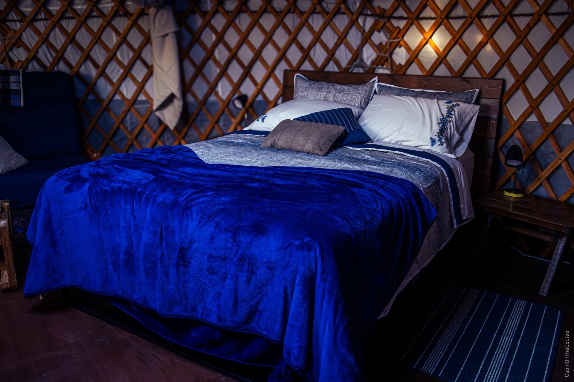 Cozy bed with blue blankets and pillows inside the yurt’s lattice interior.