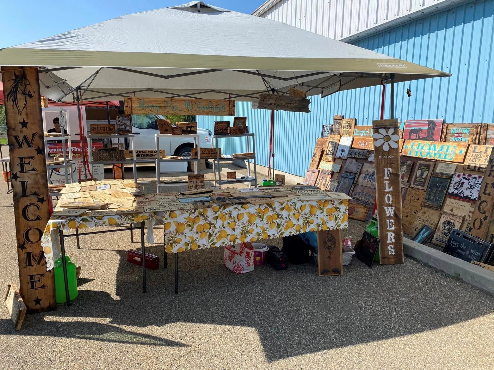Outdoor vendor booth with handmade wooden signs and crafts at Mulhurst Bay Farmers’ Market.