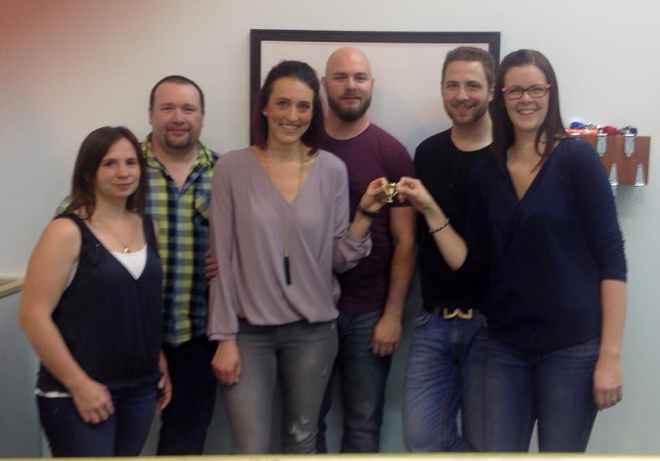 Group of six people posing in front of framed wall sign, indoors.