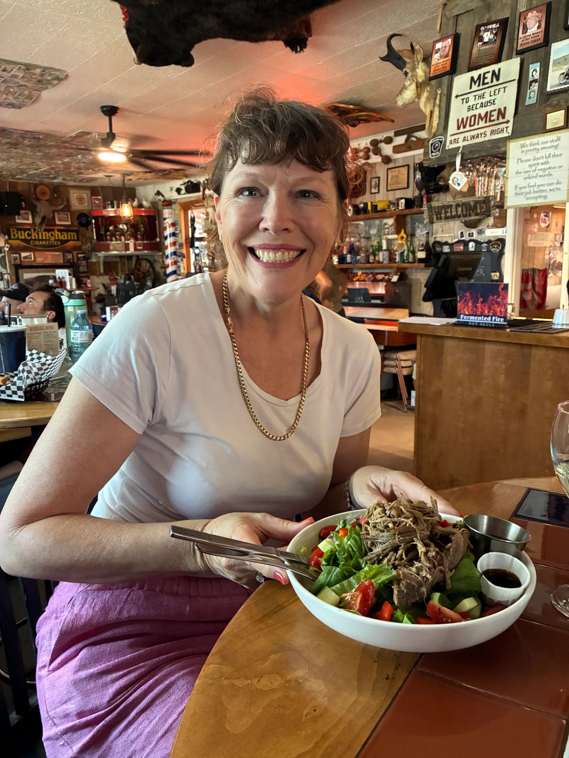 Smiling diner holding salad with shredded meat in eclectic, memorabilia-filled restaurant interior.