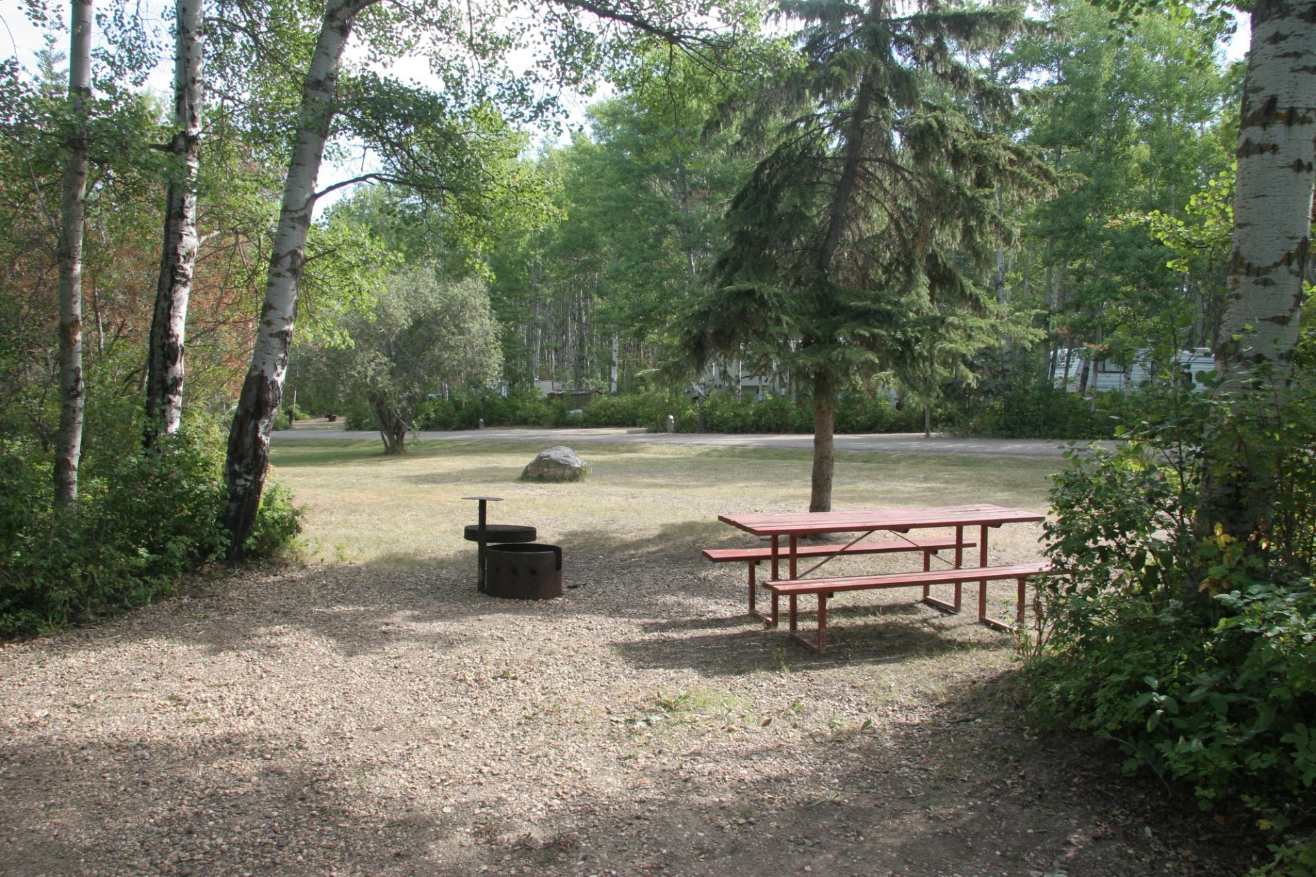 Campsite with red picnic table, metal fire pit and surrounding leafy trees.