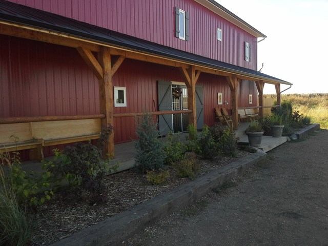 Red ranch house with porch, wooden beams, and garden plants in a rustic setting.