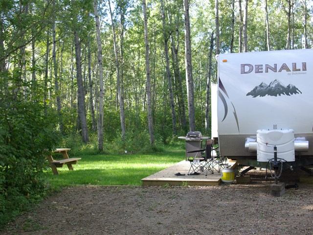 RV parked beside deck and picnic table in forested campsite at Hamilton House RV Park.