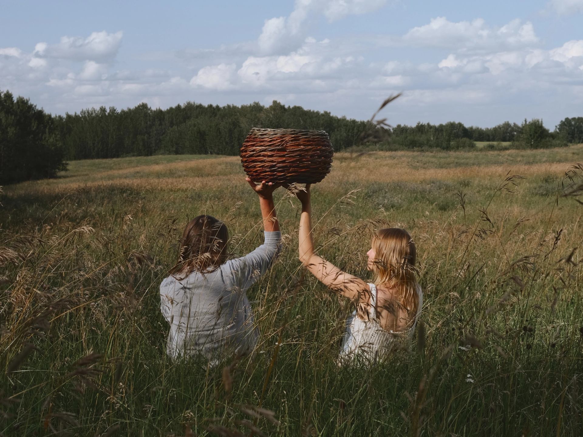 Two woman holding a basket while sitting in a meadow. 