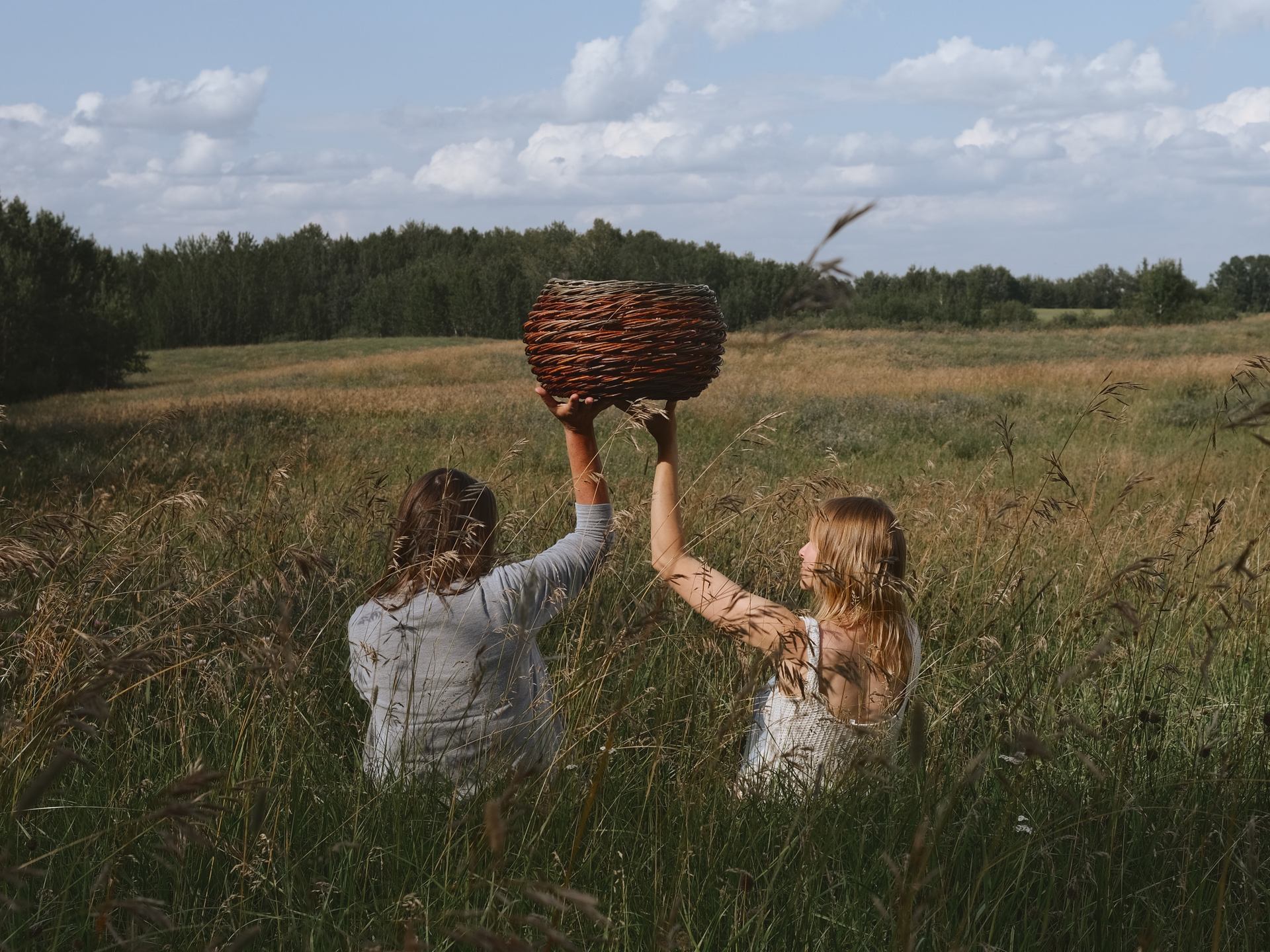 Two woman holding a basket while sitting in a meadow.