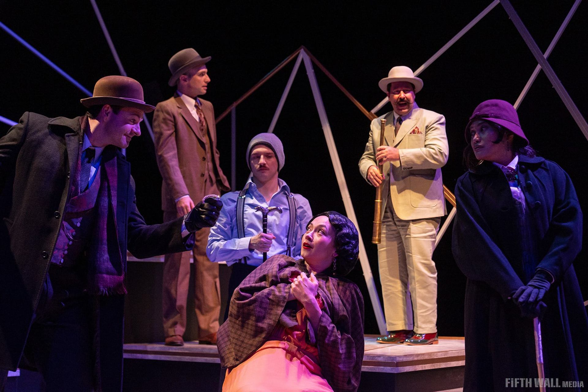 Stage actors in vintage costumes perform a dramatic scene with props against a dark backdrop.
