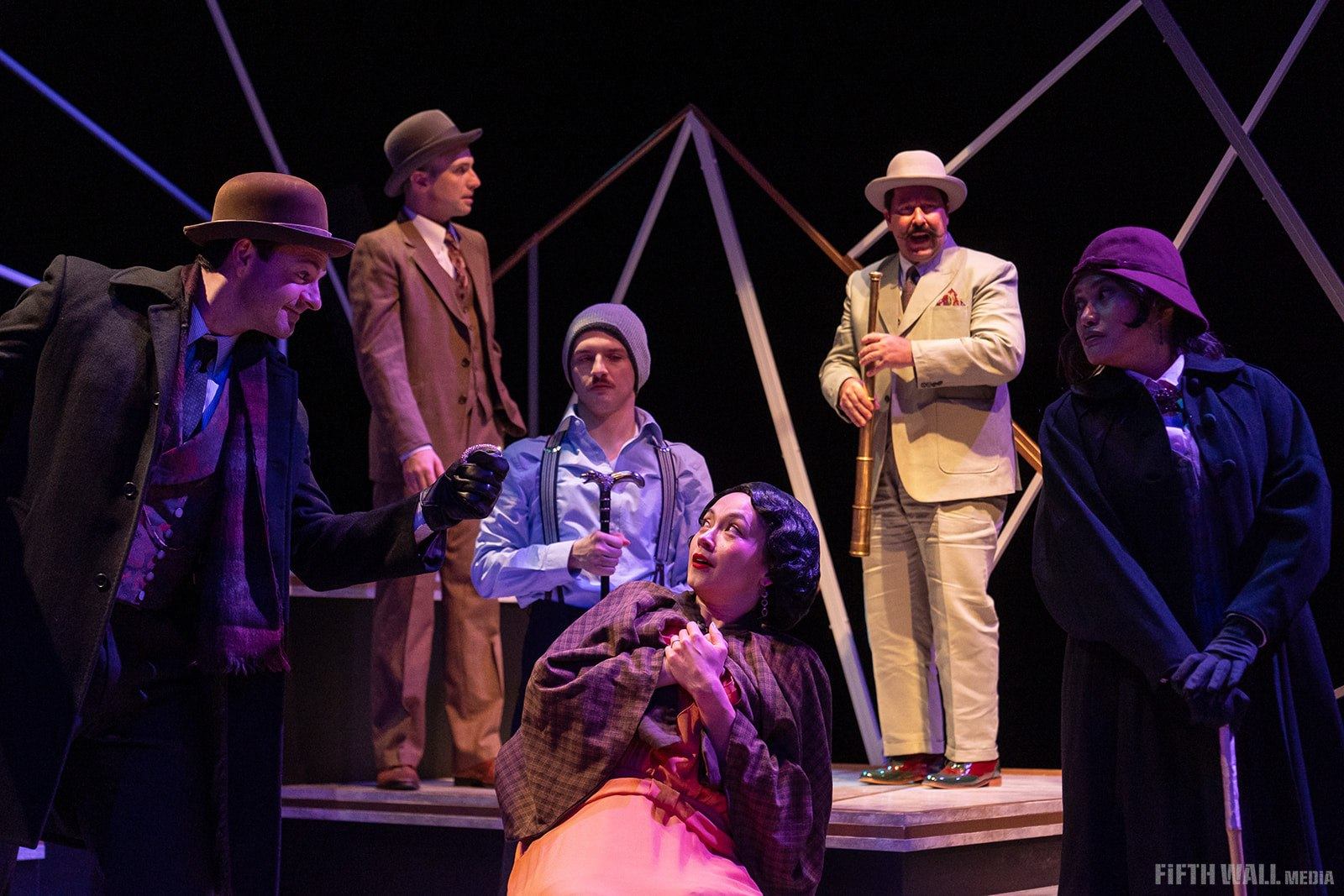 Stage actors in vintage costumes perform a dramatic scene with props against a dark backdrop.