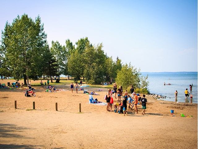 People enjoying the sandy beach and water at Sylvan Lake on a bright summer day.