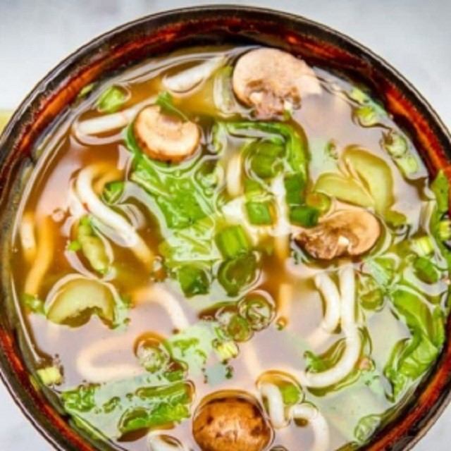 Bowl of pho with mushrooms, greens, and noodles in clear broth