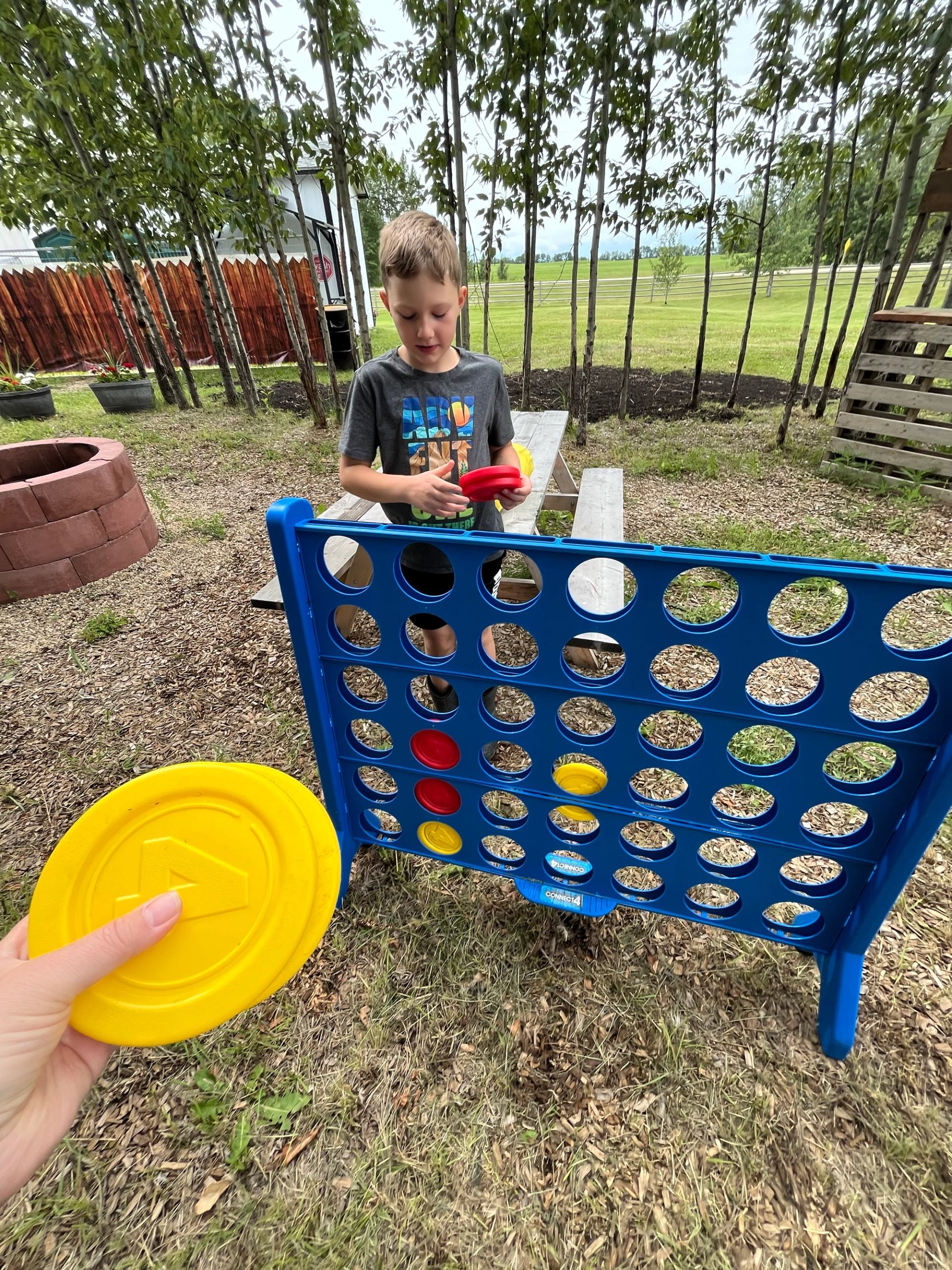 Outdoor Connect Four game with colorful discs and a child standing behind the board.