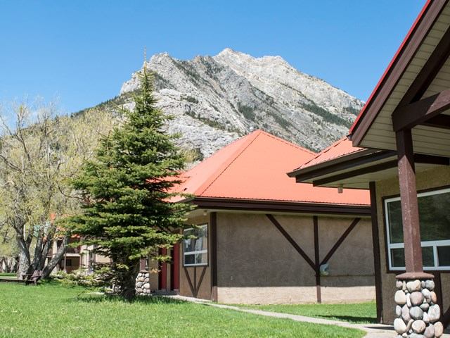 Scenic inn with red roofs, green lawn, and mountain backdrop under blue sky.
