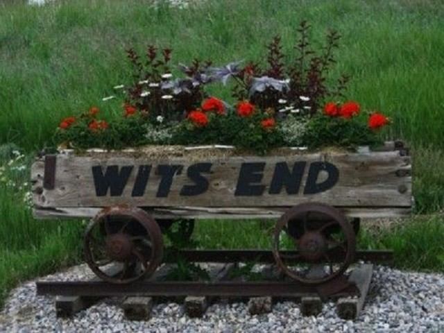Flower-filled wooden cart on tracks with “WITS END” painted on the front.