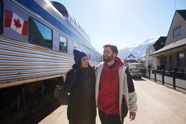 Couple walking beside a Via Rail train about to board.