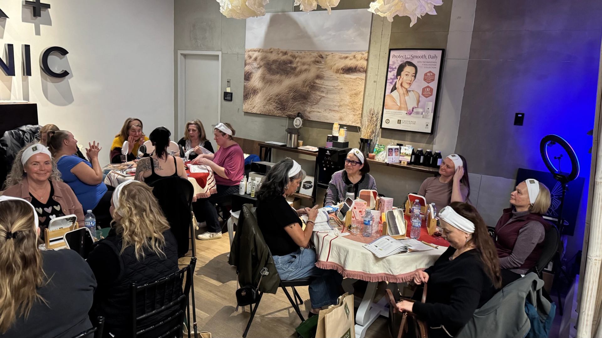 People wearing headbands sit around tables at a skincare workshop with mirrors and products.