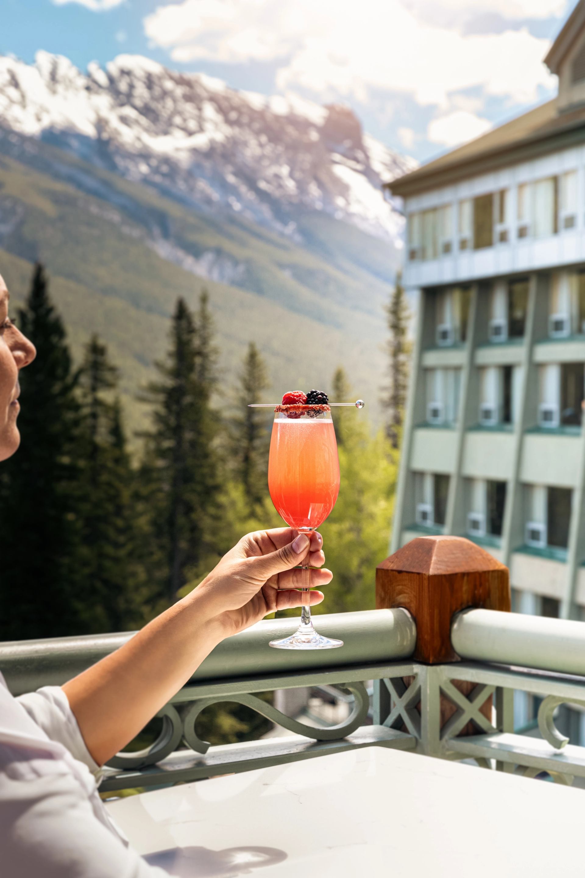 Woman holding colourful cocktail up to the mountain views