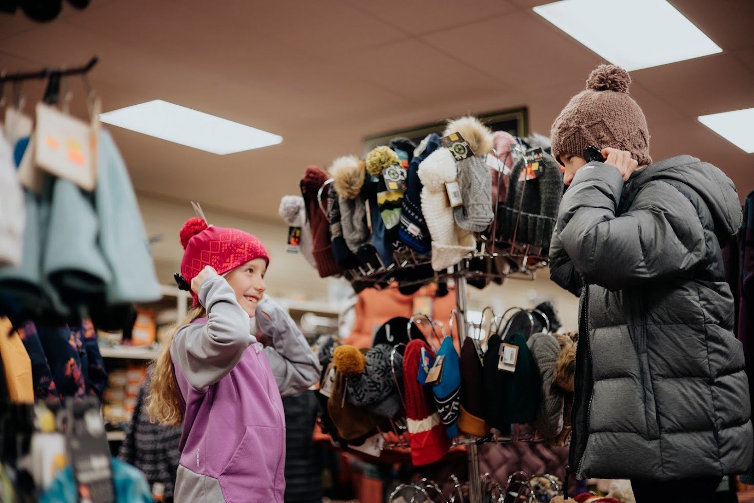 Shoppers try on knit winter hats beside a store display of colourful toques.
