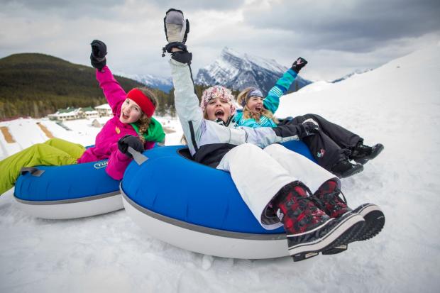 A group of children at the top of the run, hands in the air, before tubing at the Tube Park at Mount Norquay in Banff National Park