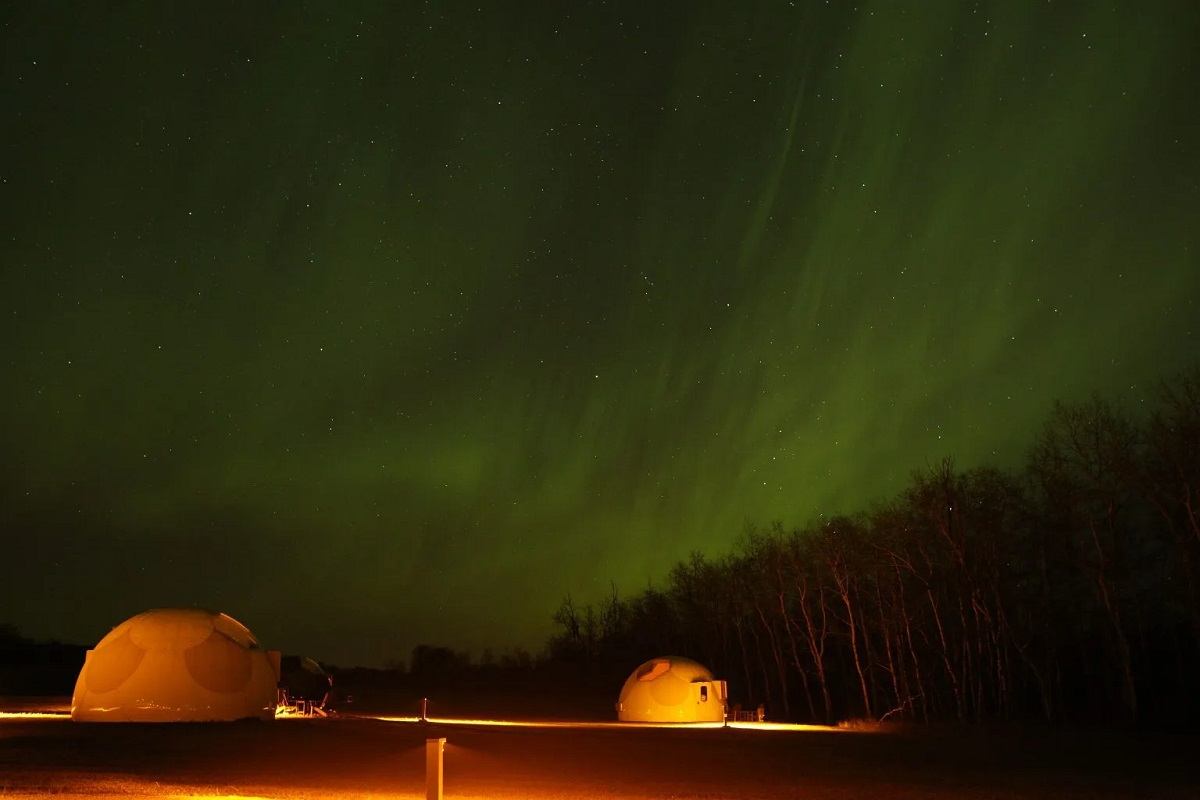 Sky domes glow beneath green aurora.