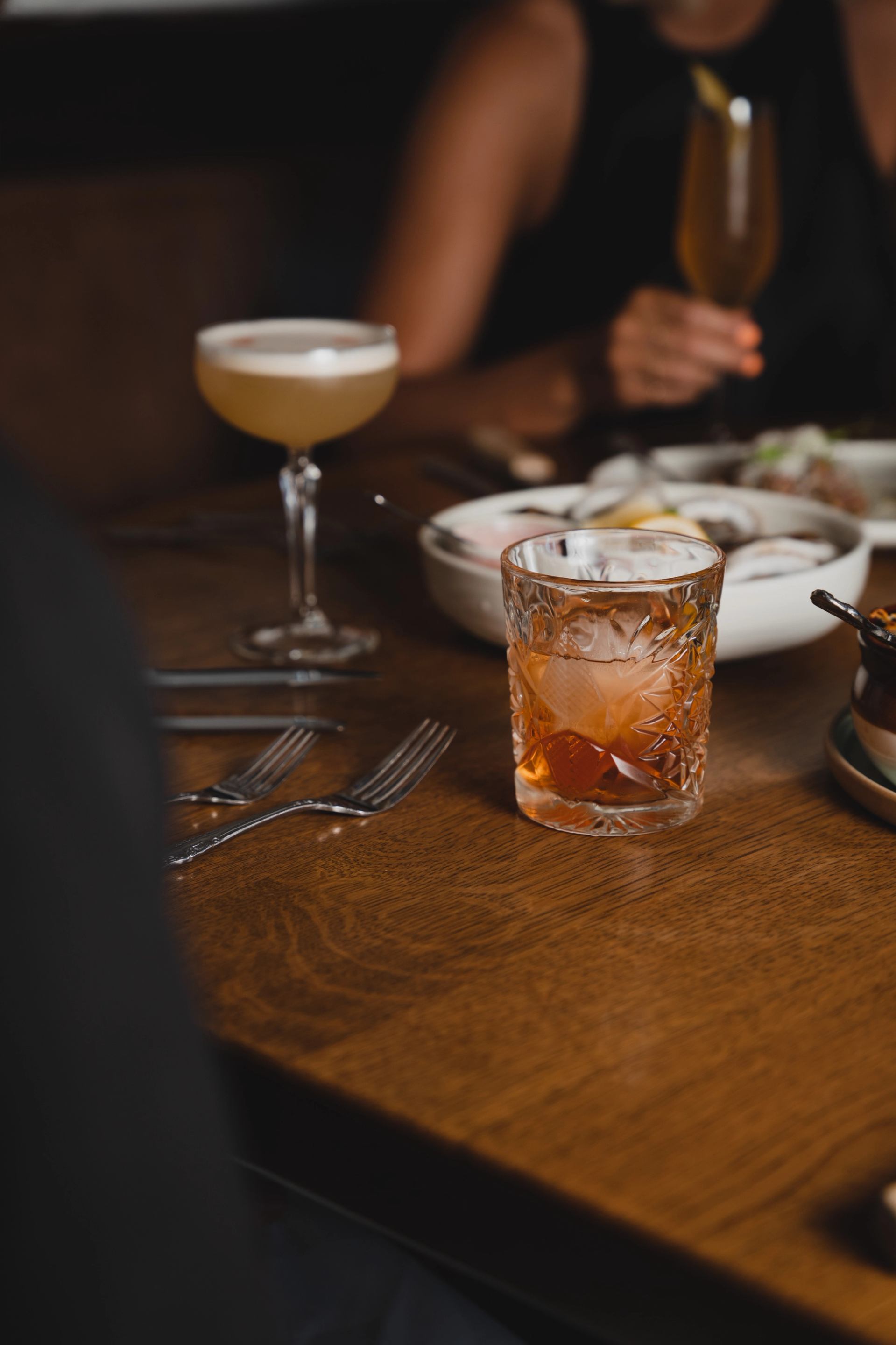 A table with cocktails and shared dishes at a restaurant setting.