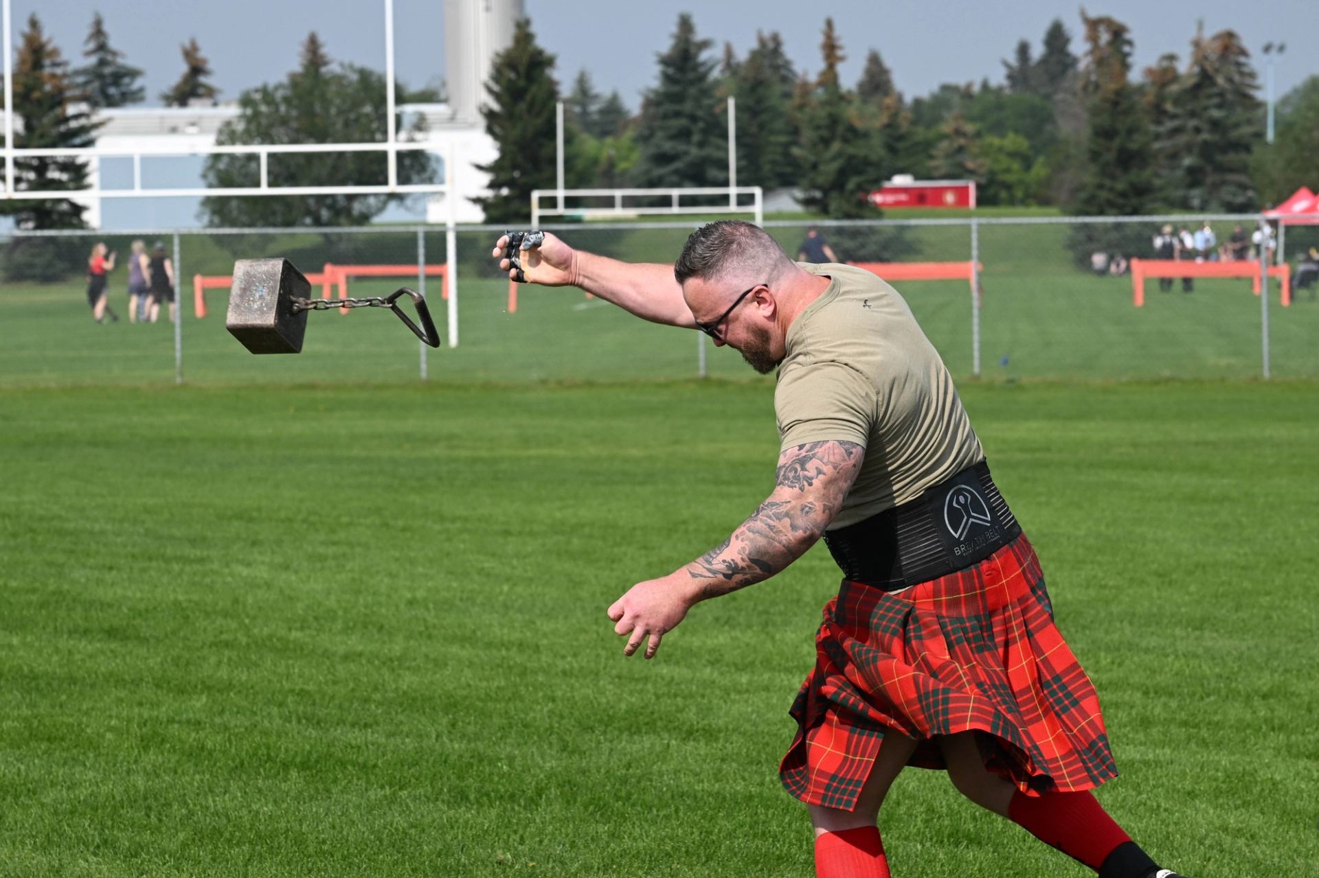 Athlete in tartan kilt throws weight at Highland Games event.