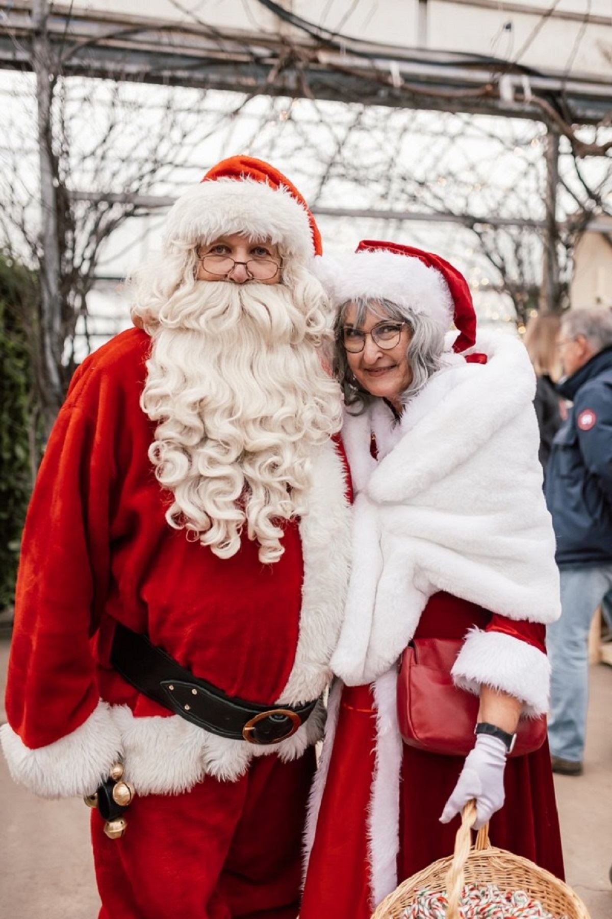 Santa and festive companion in holiday attire at outdoor Christmas market.
