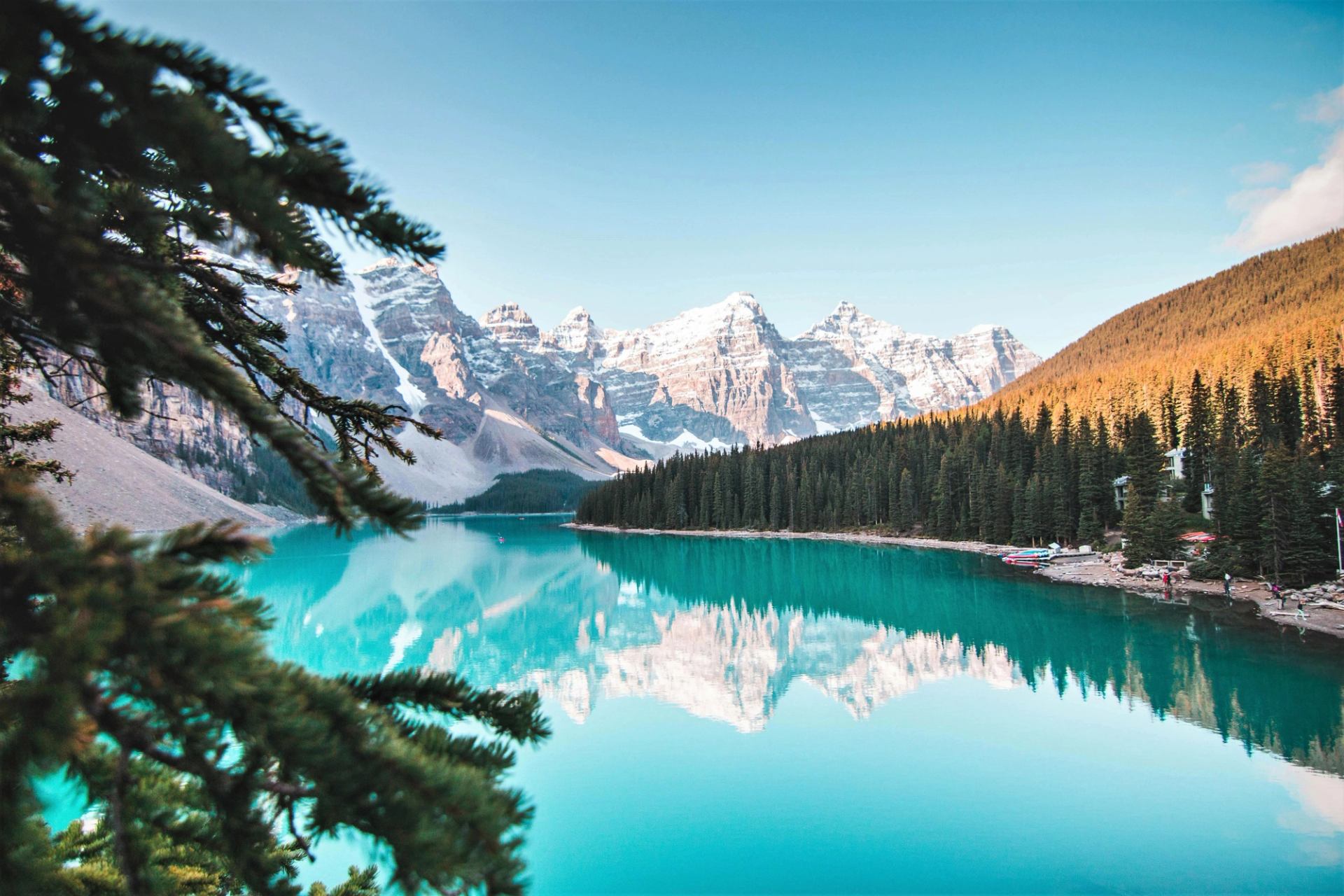 Turquoise mountain lake with snow-capped peaks, evergreen forest and small boats along shore.