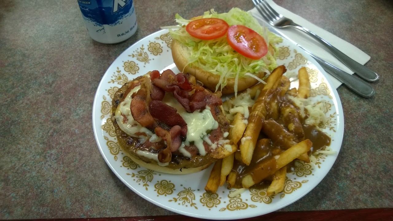 Plate with bacon cheeseburger topped with lettuce and tomato, served with poutine and gravy.